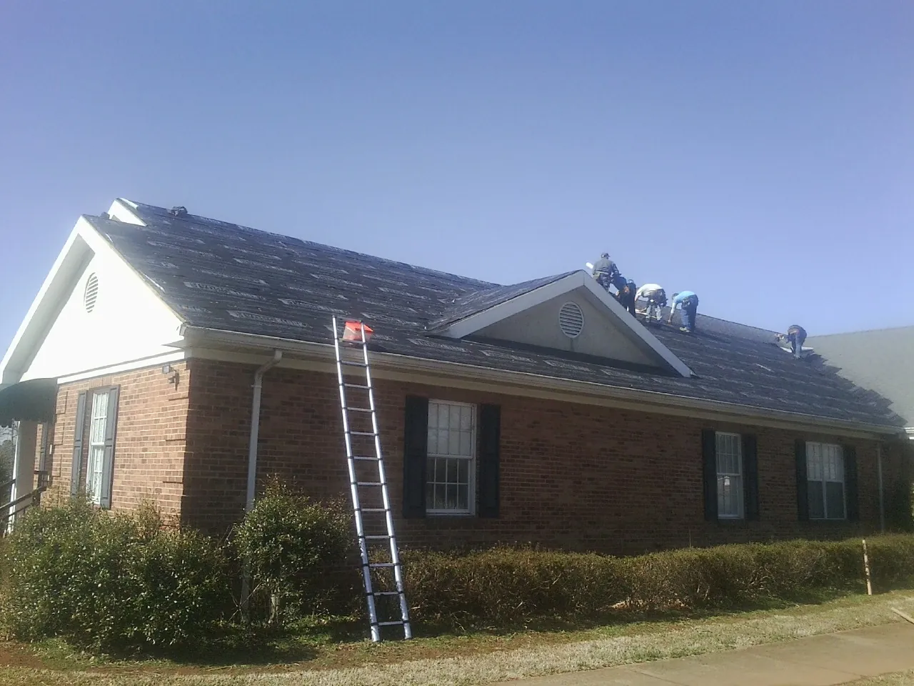 Crew tearing shingles off a brick ranch roof with a ladder set — Metal Roof Repair work by our crew in Decaturville