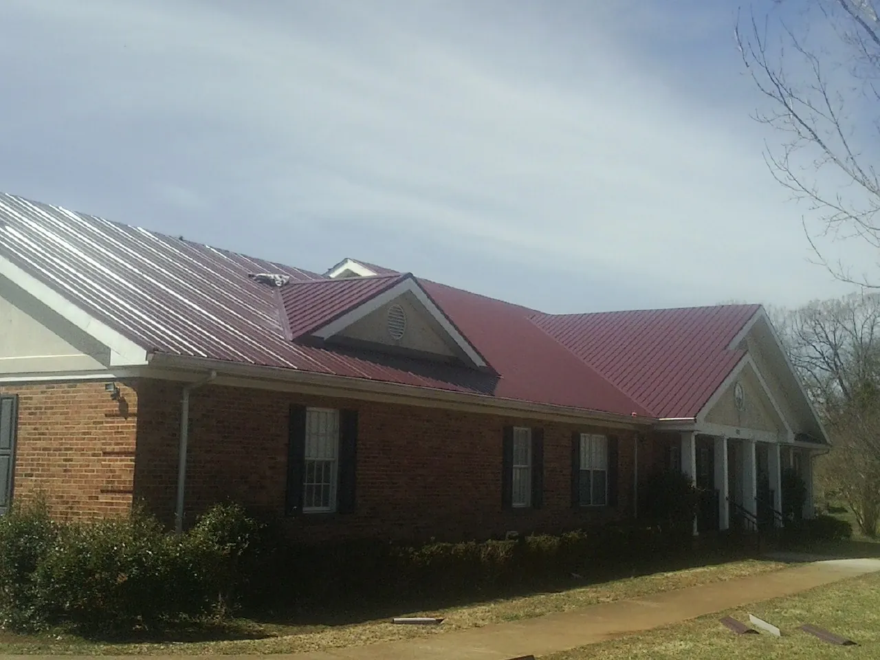 Red metal roof with gabled entries on a long brick building, from a Hail Damage Roof Repair job in Decaturville