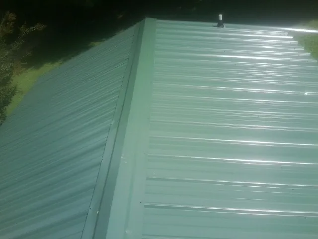 New green metal panels meeting at the ridge of a roof — Flat Roof Repair work by our crew in Decaturville