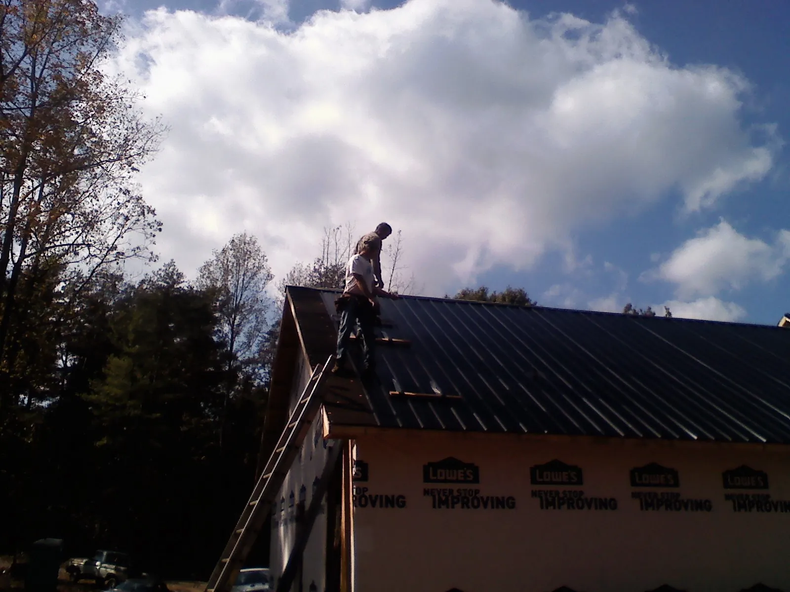 Roofer fastening dark metal panels high against a cloudy sky, from a Roof Inspection job in Decaturville