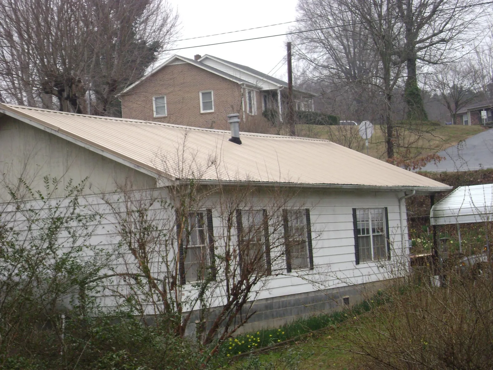 Tan metal roof on a white sided house set into a hillside — Commercial Roofing by Roofing Brothers in Decaturville