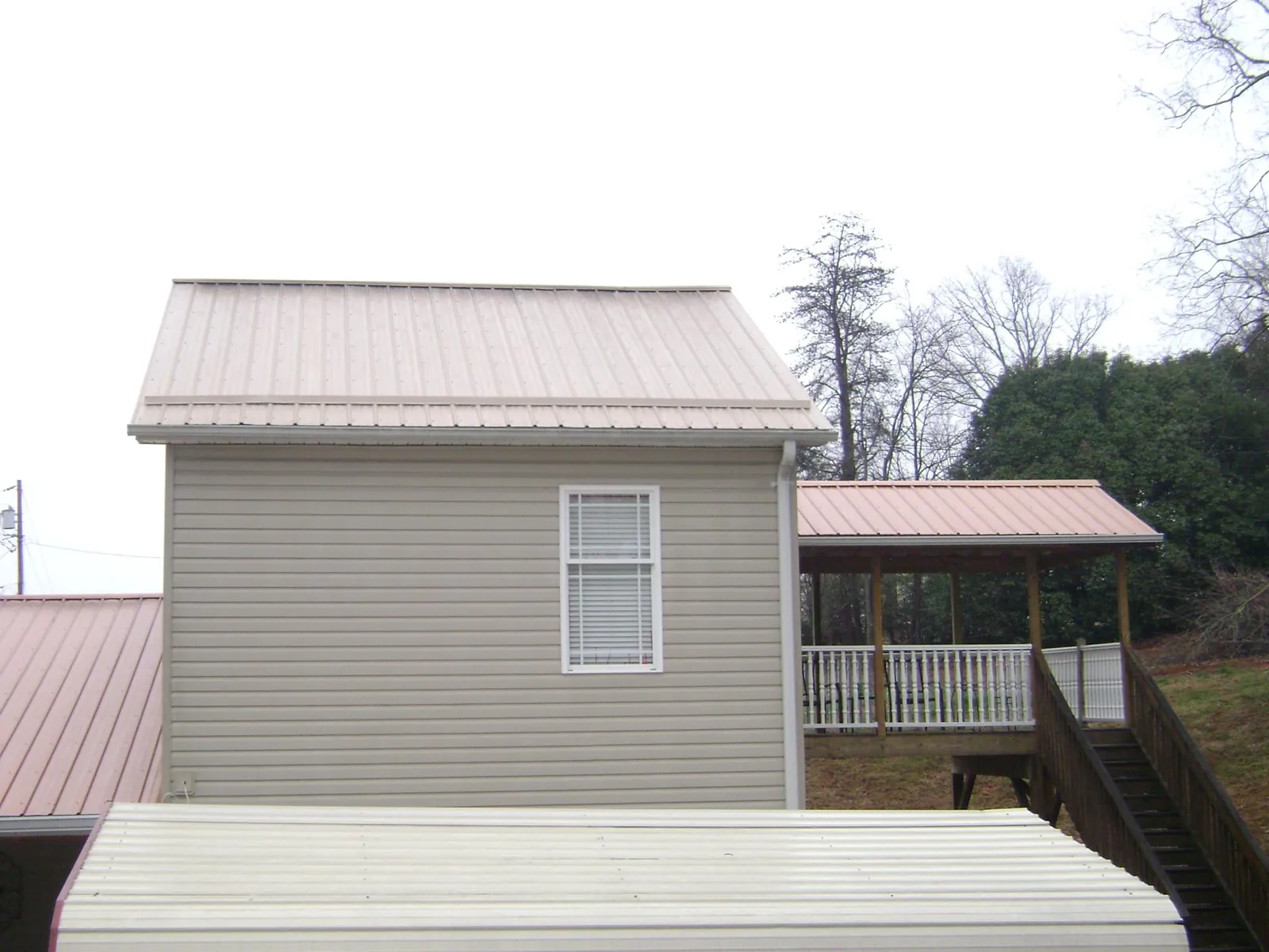 Tan metal roofs on a two story addition and attached porch, from a Roof Replacement job in Decaturville